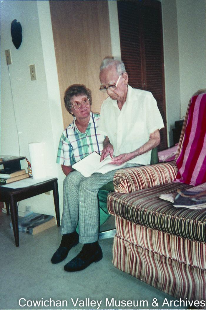 [Unidentified elderly man and woman sitting and reading a book]