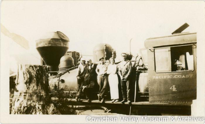 [A group of four men and one women posing with a locomotive]