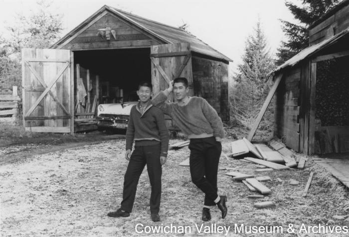 [Two men posing in front of a car garage]
