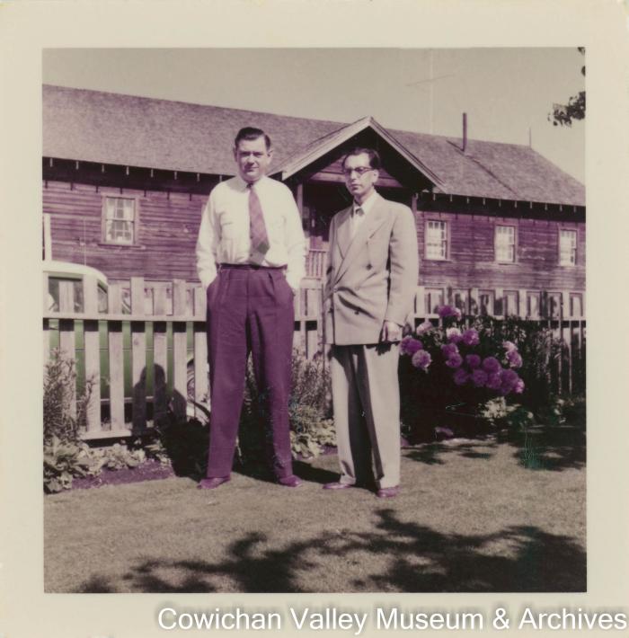[Two men in suits posing for a photo in a garden]