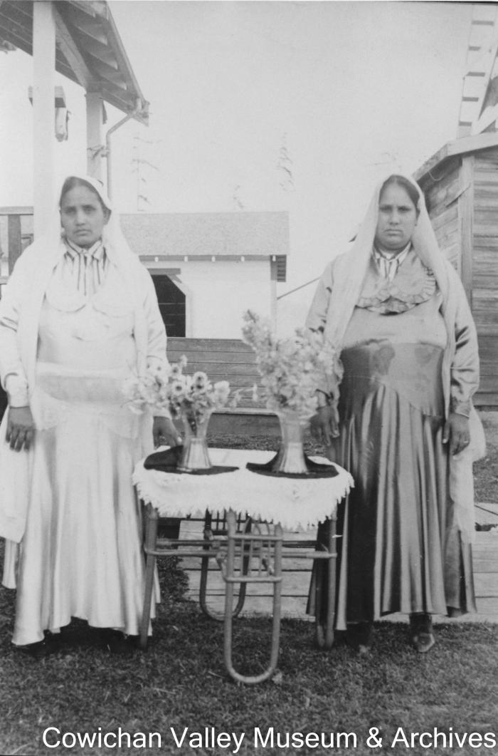 [Two women standing next to flowers on a table]