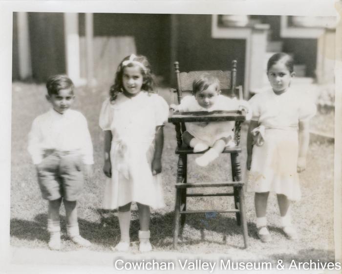 [Four young children including an infant in a high chair posing for a photo]