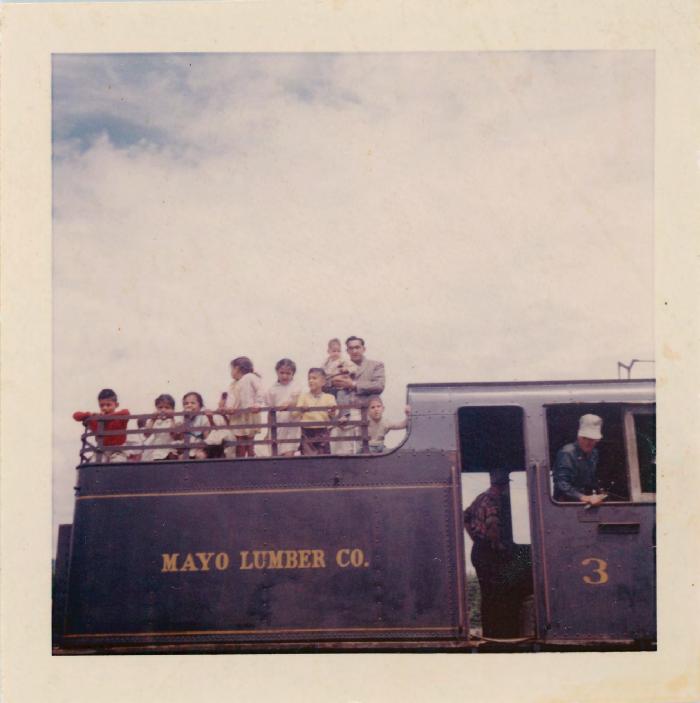 [Photo of Rajindi Mayo and Clarence Martin with a group of children on a steam engine]