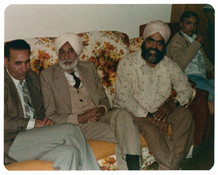 [Photo of Nirmal Singh with a group of men inside a house]