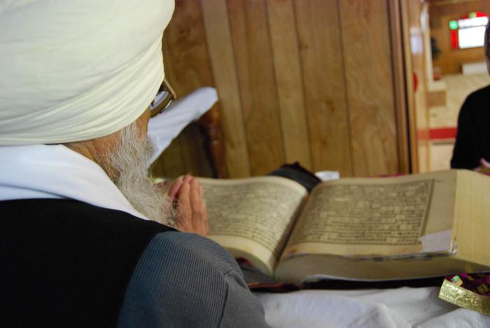[Photo of a Sikh man praying in front of the Sri Guru Granth Sahib]
