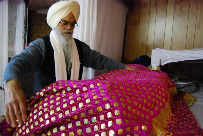 [Photo of a South Asian man covering the Guru Granth Sahib]