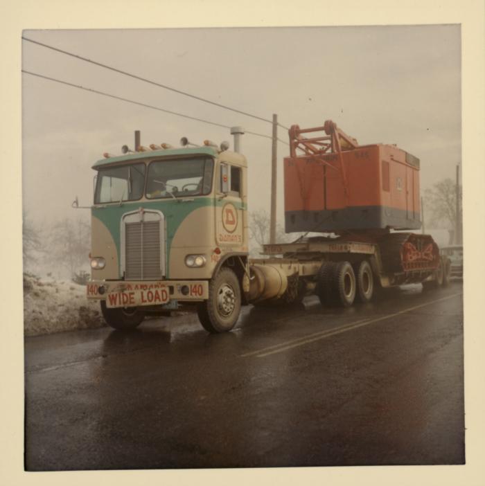 [Yellowed photo of Doman Industries transport truck no. 140 hauling the chassis of a construction vehicle]