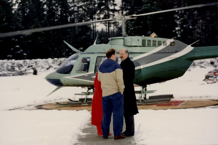 [Photo of Mike Harcourt speaking with two unidentified people near a helicopter]