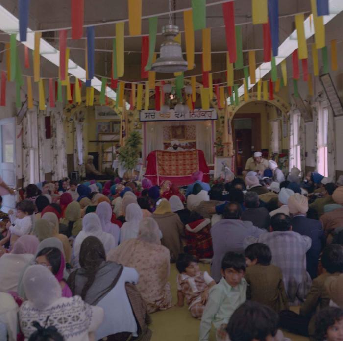 [Photo of the wedding guests facing the Granthi at the front of the Gurdwara]