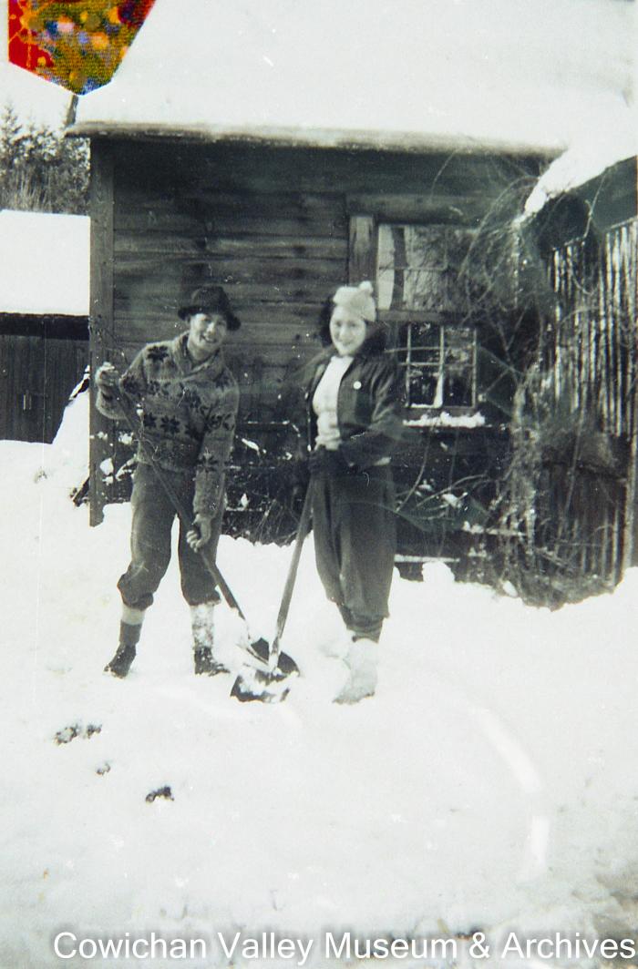 [Two unidentified adults in the snow holding shovels]