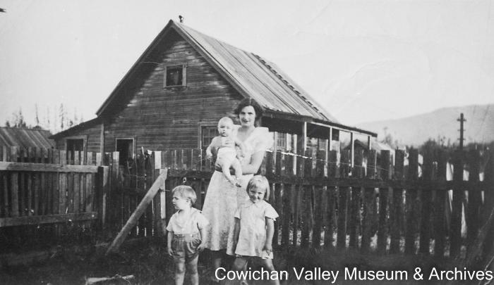 [Unidentified mother with three children in front of wood fence]