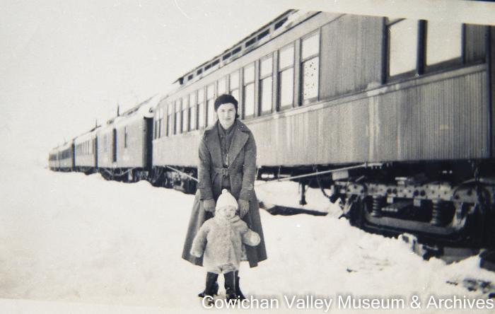 [Unidentified woman and child standing in the snow near a train]