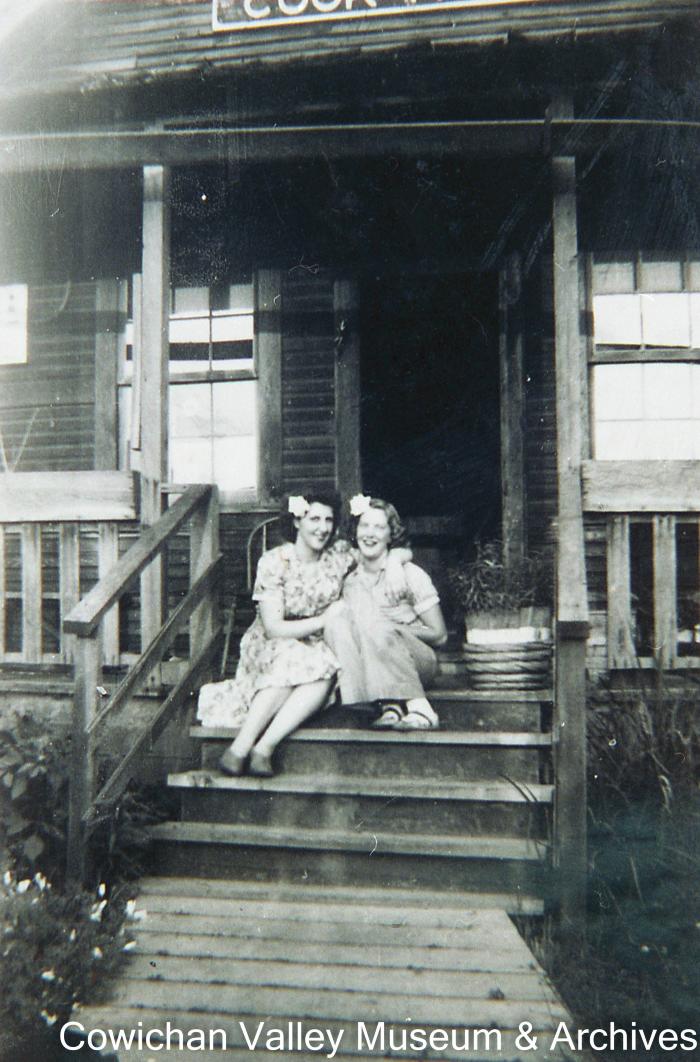 [Two unidentified women with flowers in their hair sitting on a porch]