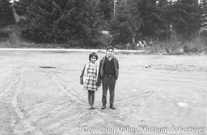 [Two unidentified children standing on a dirt road]