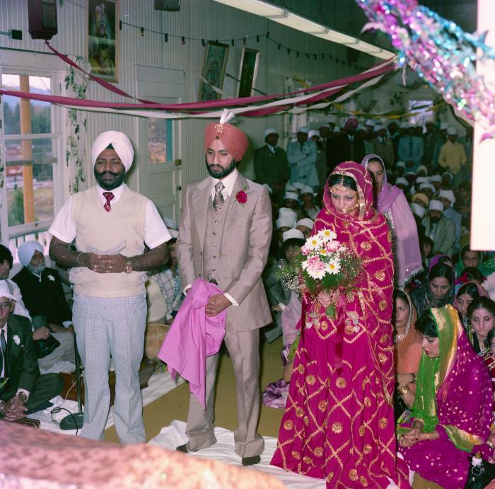 [Group photo of Jagpal Davinder and Manjit Sarowa with Head Granthi standing and doing Ardās in front of the Sri GuruGranth Sahib]