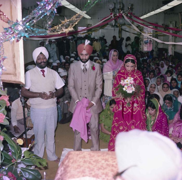 [Group photo of Jagpal Davinder and Manjit Sarowa with Head Granthi standing and doing Ardās in front of the Sri GuruGranth Sahib]