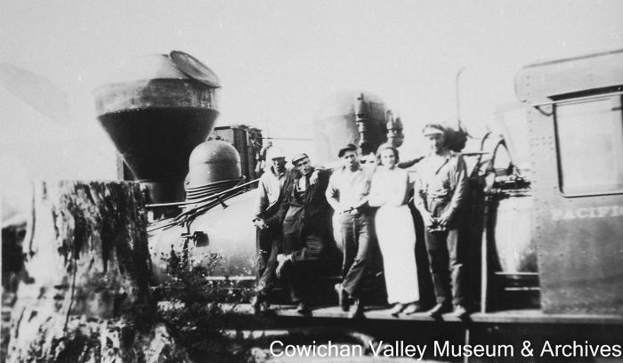 [Four unidentified men and one unidentified woman standing  on railroad locomotive]