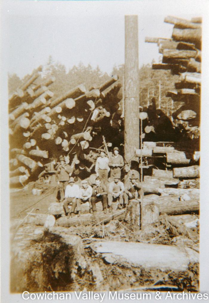 [Group of loggers posing infront of stacks of logs]